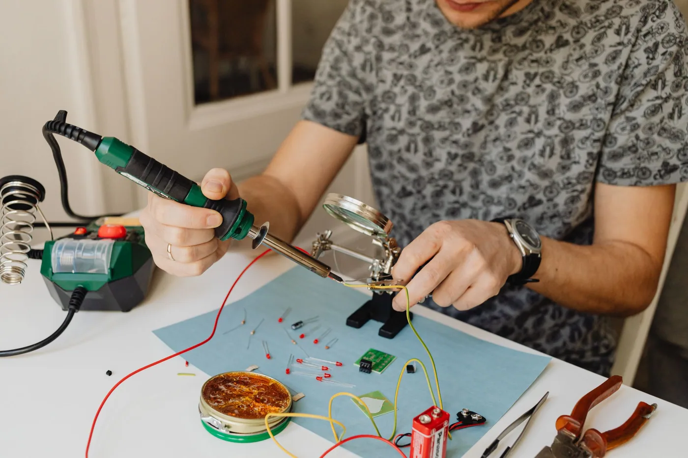 An engineer soldering components onto a small circuit board at an electronics workbench.