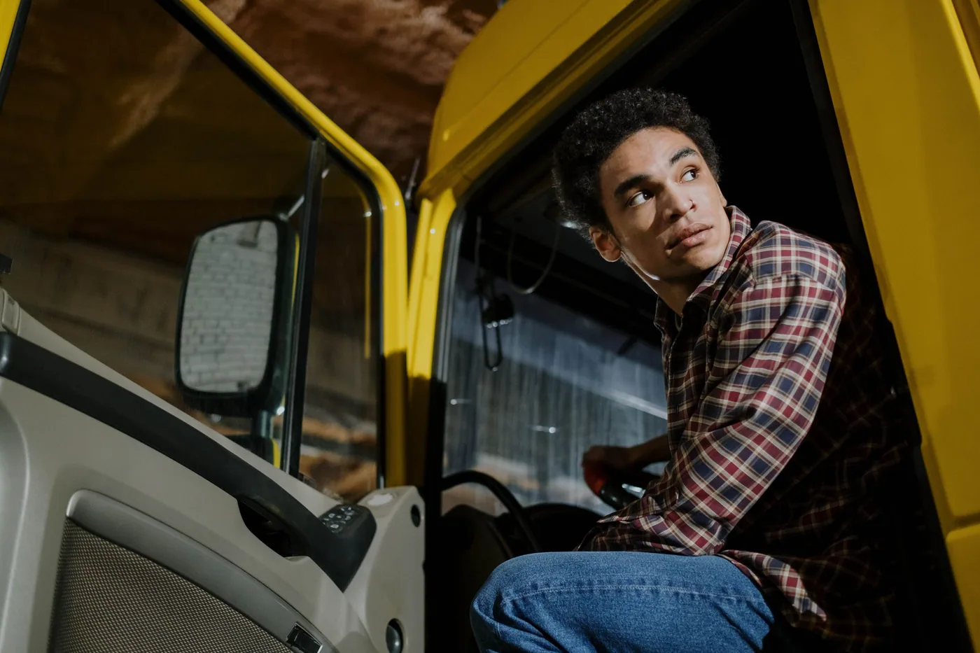A driver seated in a truck cab holding a handheld device, seen from the passenger side.