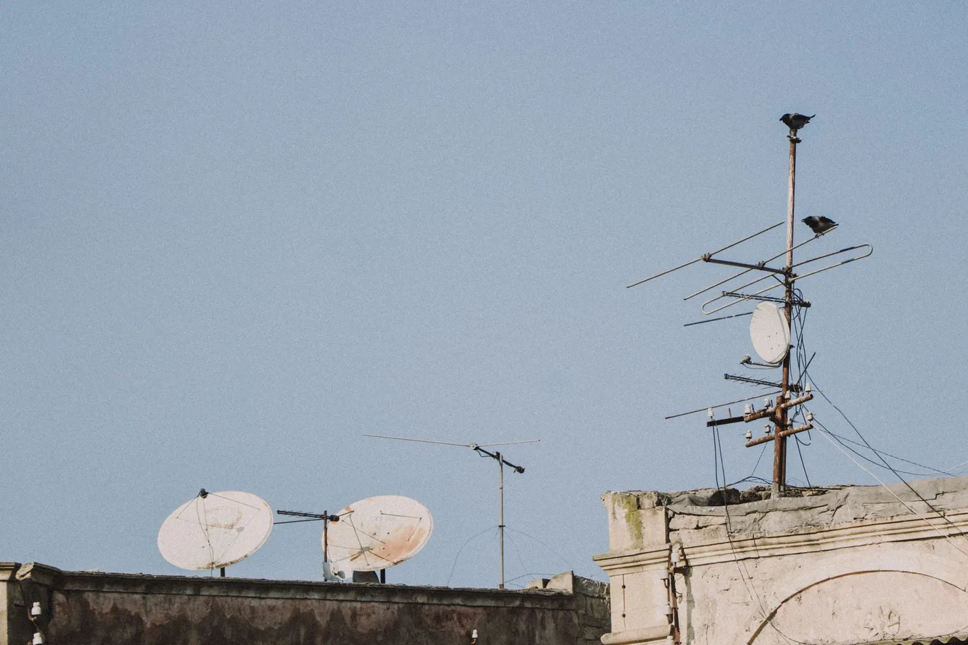 Sector and whip antennas mounted on a rooftop mast with feeder cables and mounting brackets against a grey sky.