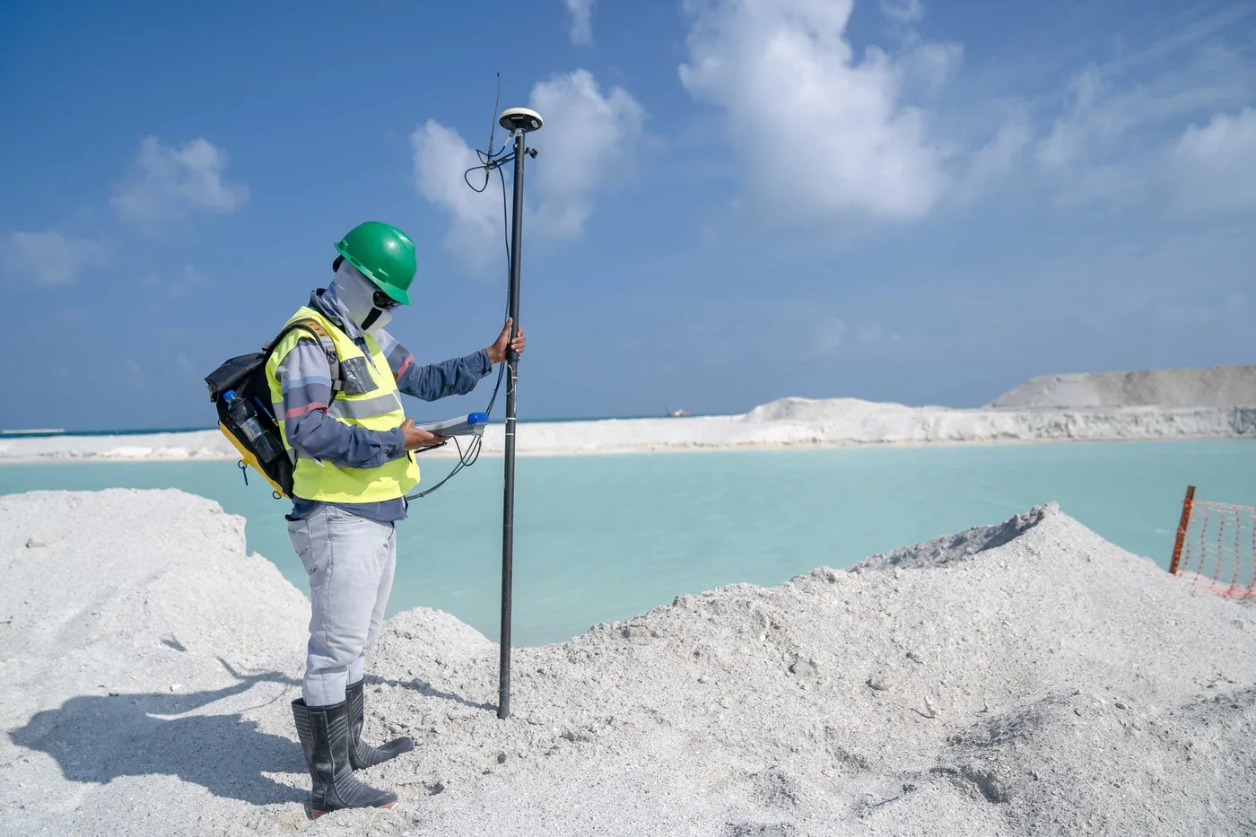 A surveyor operating a tripod-mounted GNSS receiver in an open field.
