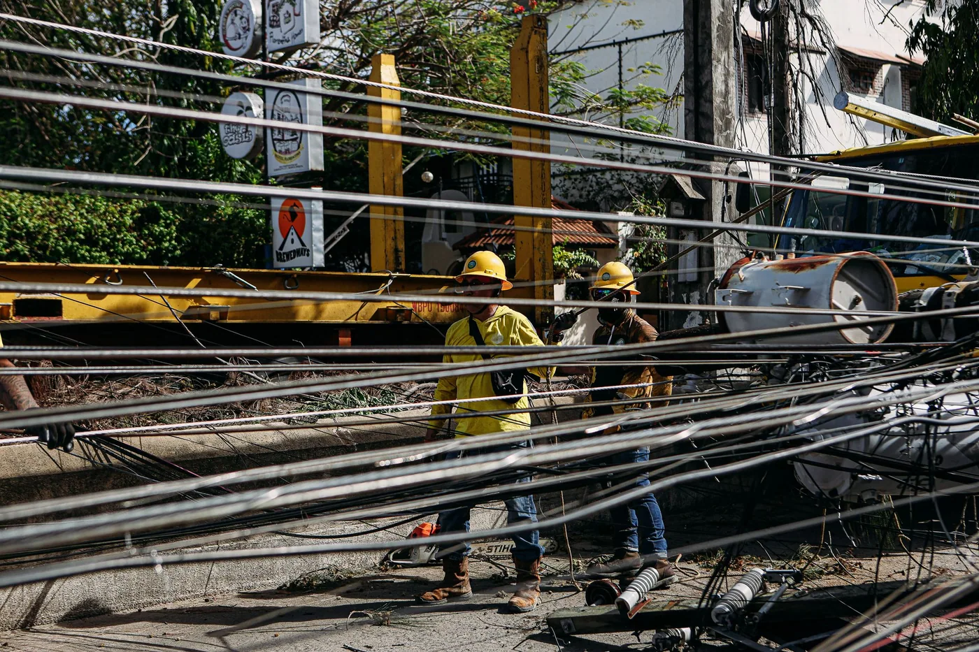A lineworker wearing a harness working on equipment at the top of a wooden distribution pole.